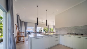 Une cuisine moderne dotée d’un grand îlot central, de meubles blancs et offrant une vue sur l’océan.