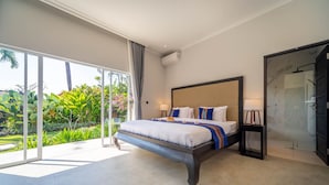 Une chambre dotée d’un grand lit, d’une porte-fenêtre coulissante donnant sur un balcon, d’un espace douche et offrant une vue sur une végétation luxuriante.