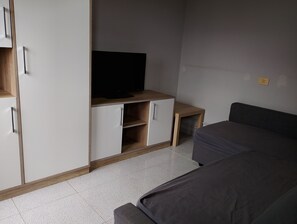 A bedroom with a bed, a TV on a wooden stand, and a wardrobe.