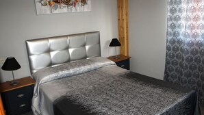 Een slaapkamer met een bed, twee nachtkastjes, een lamp op elk kastje, een kunstwerk aan de muur en een gordijn met patroon.