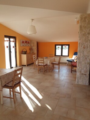 A dining area with a table and chairs, a kitchen area with cabinets and a window, and a stone wall.