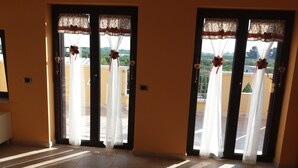 A hotel room with a view of a balcony, a tiled floor, and a door with a white curtain and a red bow.