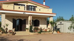 A two-story house with a tiled roof, a stone facade, and a paved driveway.