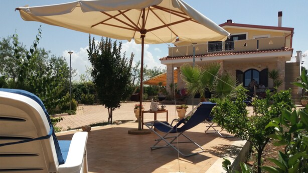 A patio area with a white lounge chair, a beige umbrella, and a stone table.