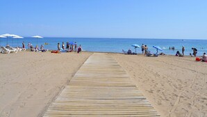 Une plage avec une promenade en bois menant à l’eau, des chaises longues et des parasols.