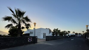 A modern building with a stone wall entrance, palm trees, and a clear sky.