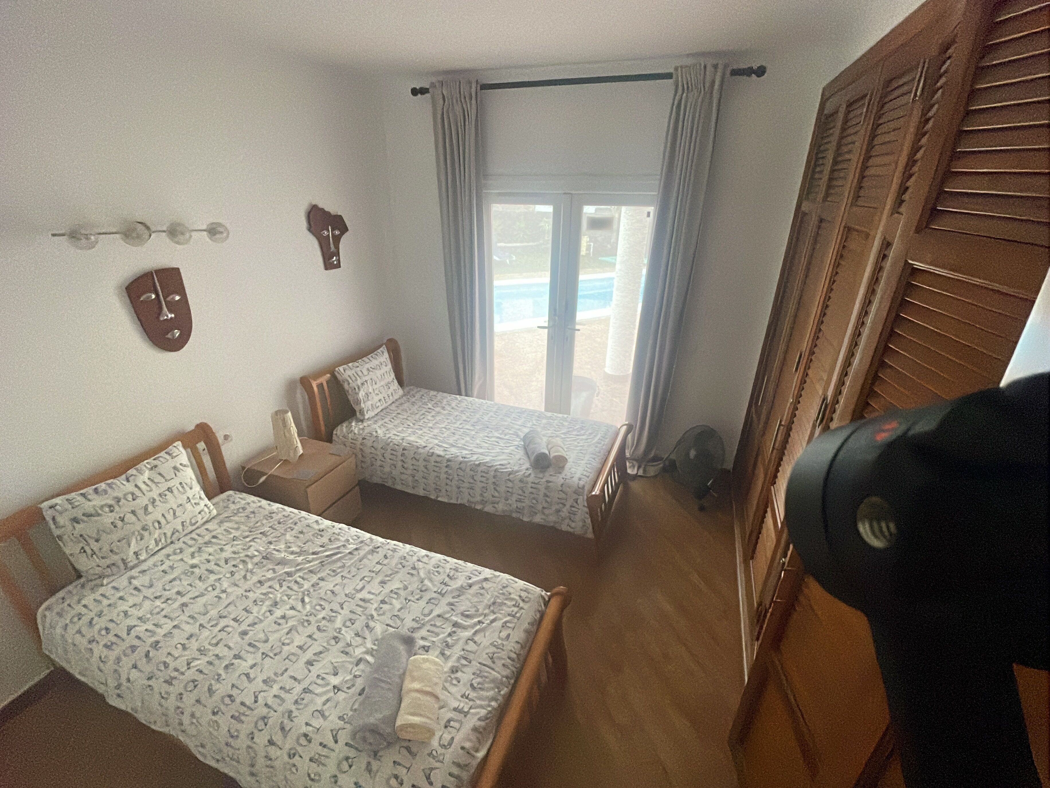 Una habitación con dos camas, una ventana con cortinas, un armario de madera y un ventilador de pared.