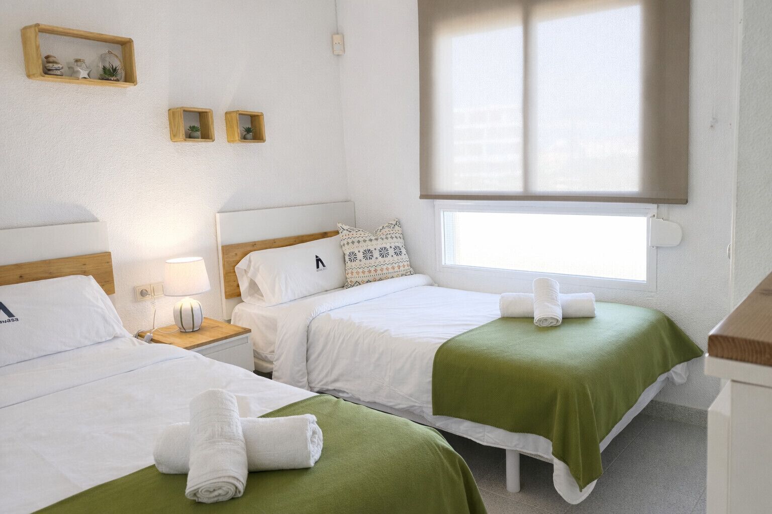 Une chambre d’hôtel avec deux lits, une fenêtre et une table de chevet avec une lampe.