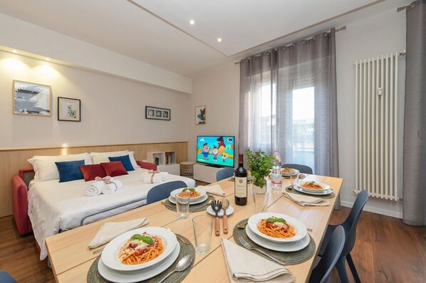 Une chambre d’hôtel avec un lit, une télévision, une table à manger dressée avec des assiettes remplies de nourriture et une fenêtre avec des rideaux.