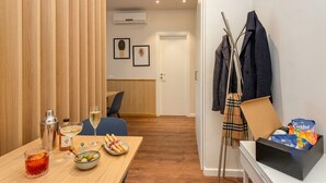 Una habitación con un separador de madera, una mesa de comedor con un cóctel, un cuenco de aceitunas y una caja de aperitivos.