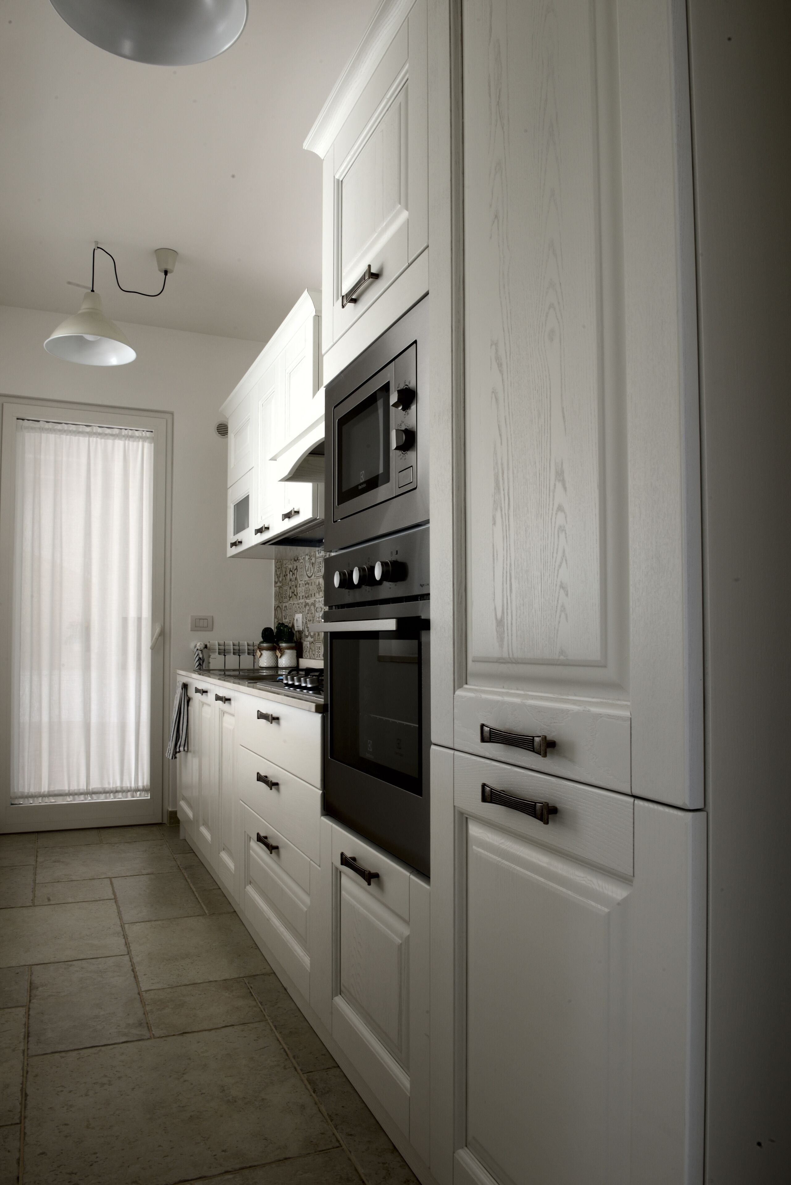 Een moderne keuken met witte kastjes, roestvrijstalen apparatuur en een betegelde vloer.