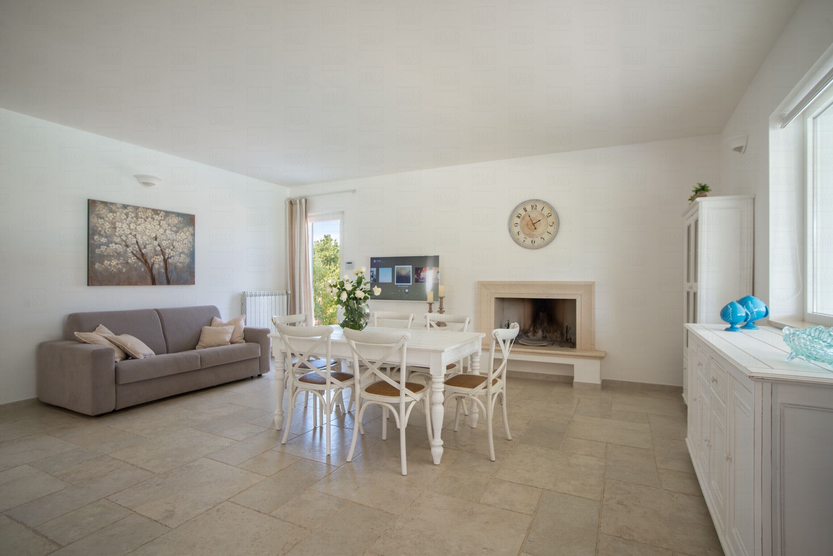 A living room with a white sofa, a dining table with chairs, a fireplace, and a clock on the wall.