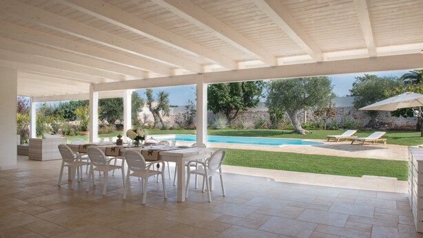 Une terrasse ouverte avec une piscine, des meubles blancs et une vue sur le jardin.