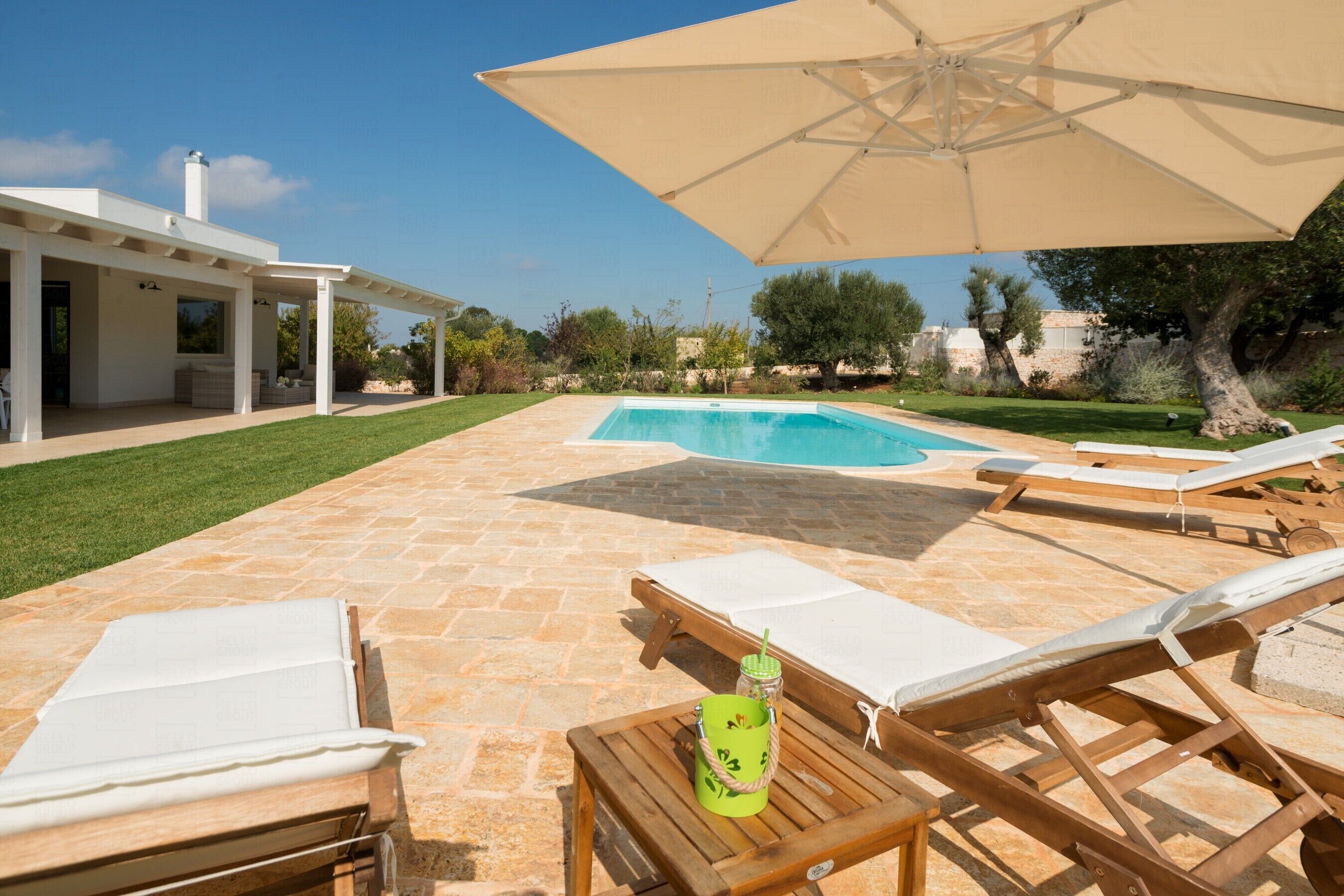 Un espace aménagé au bord de la piscine, avec des chaises longues, une table avec des boissons et une pergola.