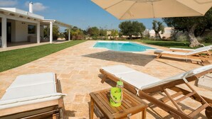 Un espace aménagé au bord de la piscine, avec des chaises longues, une table avec des boissons et une pergola.
