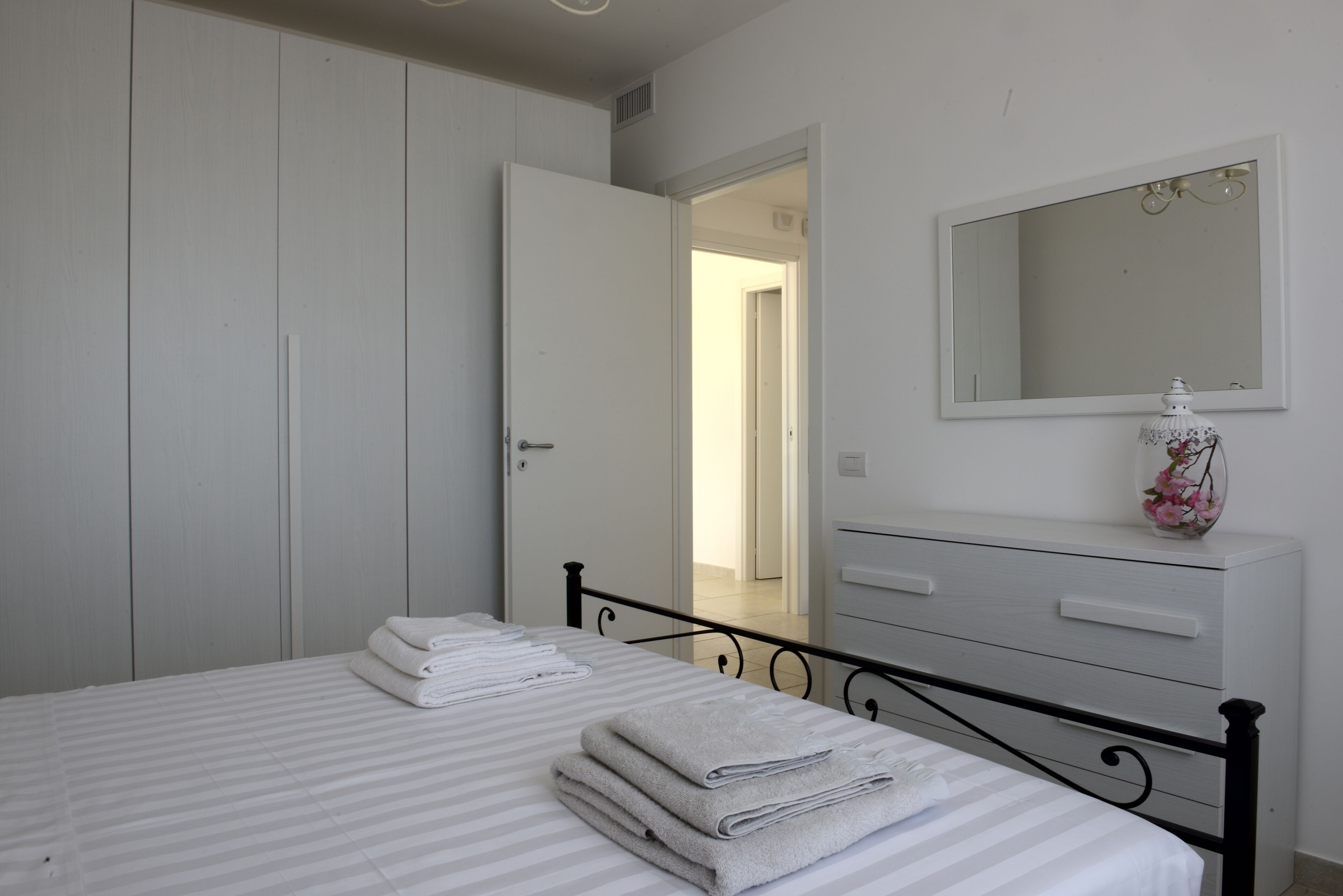 A bedroom with a bed, a dresser, a mirror, and a door leading to another room.