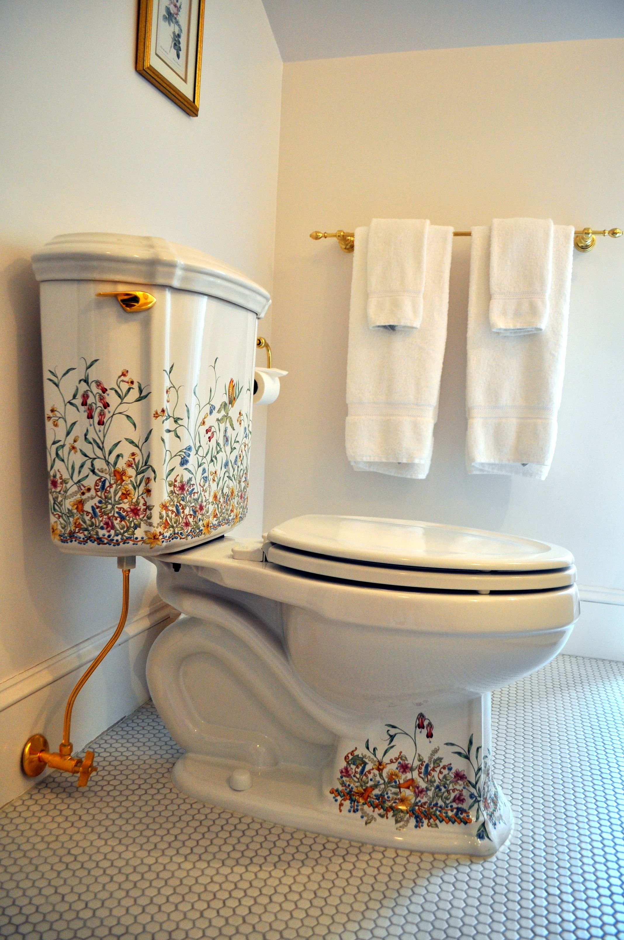 Eine Toilette mit floralen Verzierungen, einem goldenen Wasserhahn und einem Handtuchhalter mit zwei Handtüchern.