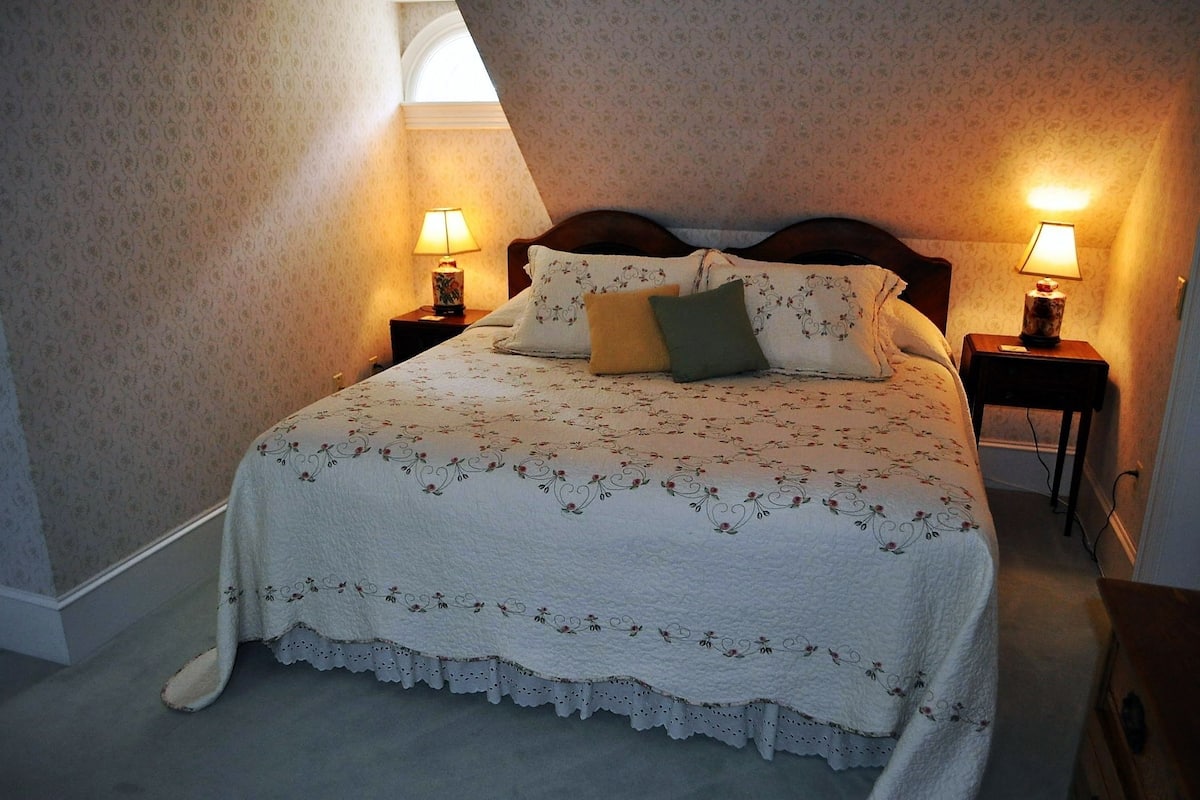 A neatly made bed with floral bedding, two bedside lamps, and a patterned wall.