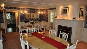 Ein Esszimmer mit einem langen Tisch, weißen Stühlen, einem Kamin und blumigem Wandpapier.