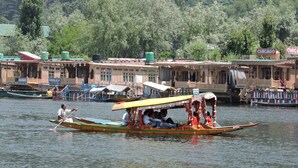 A traditional boat with passengers, a docked boat, and buildings in the background. - Appollo eleven group of houseboats (Srinagar)