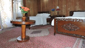 A traditional room with a wooden bed, a small round table with a vase of flowers, and a patterned carpet. - Appollo eleven group of houseboats (Srinagar)