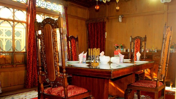A dining area with a wooden table, chairs, and a red carpet. - Appollo eleven group of houseboats (Srinagar)