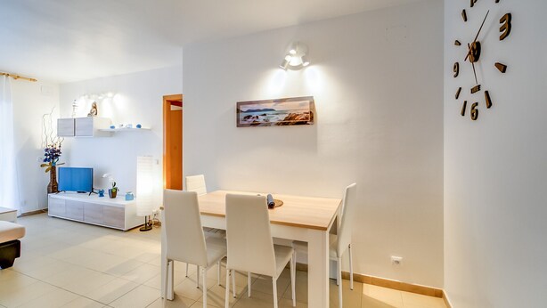 A modern dining area with a wooden table and white chairs, a painting on the wall, and a wall clock. - Apartment for 5 people, community pool 5 minutes from the beach and the promenade of Blanes, free wifi, air-conditioned living room. Vivalidays Edurne. (Blanes)