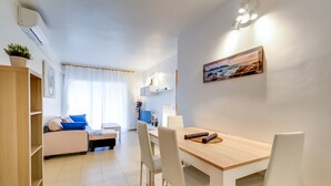 A modern living room with a sofa, a dining table with chairs, a TV, and a painting on the wall.