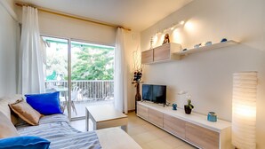 A modern living room with a sofa, TV, and a balcony with a view of trees.