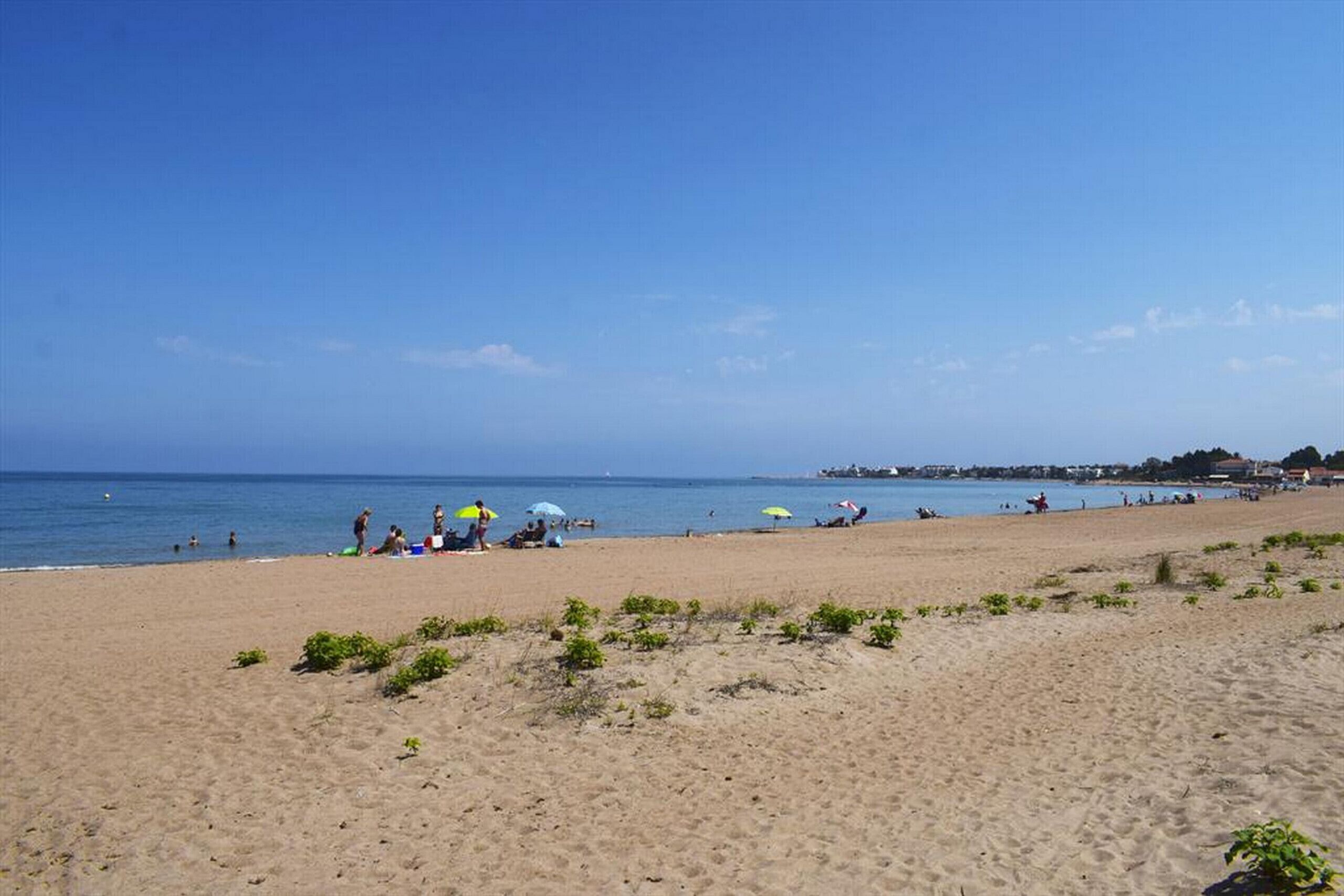 A beach with people, umbrellas, and a clear sky.