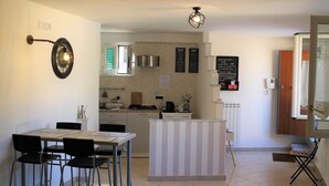 A compact kitchen with a dining area, a small refrigerator, and a coffee machine.