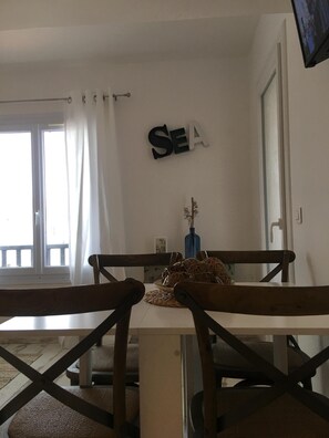 A dining area with a table and chairs, a vase with dried plants, and a wall sign that reads "SEA". - APARTMENT "le Méditerranéen", 2 bedrooms and all comforts, 300m from the sea (Saintes-Maries-de-la-Mer)