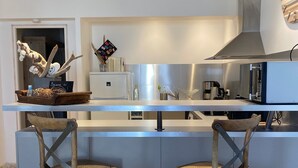 Una cocina moderna con una isla central, dos taburetes de bar, una campana extractora de acero inoxidable y una rama decorativa de algodón.