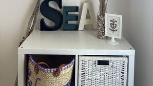 Una habitación con un armario blanco que exhibe objetos decorativos, entre ellos una cesta tejida y un jarrón con plantas secas.