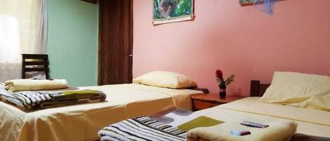 A hotel room with two beds, a wooden ceiling, and a window with curtains.