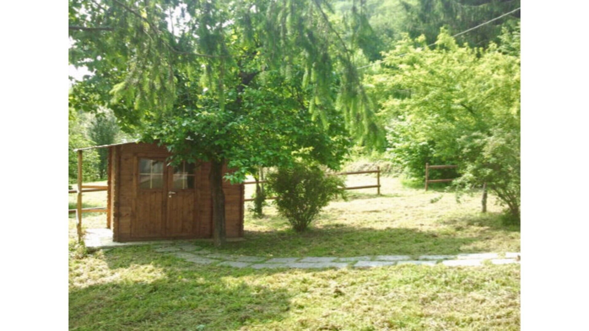 A small wooden cabin with a window, surrounded by a grassy area and trees.
