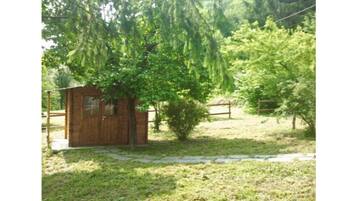 A small wooden cabin with a window, surrounded by a grassy area and trees.