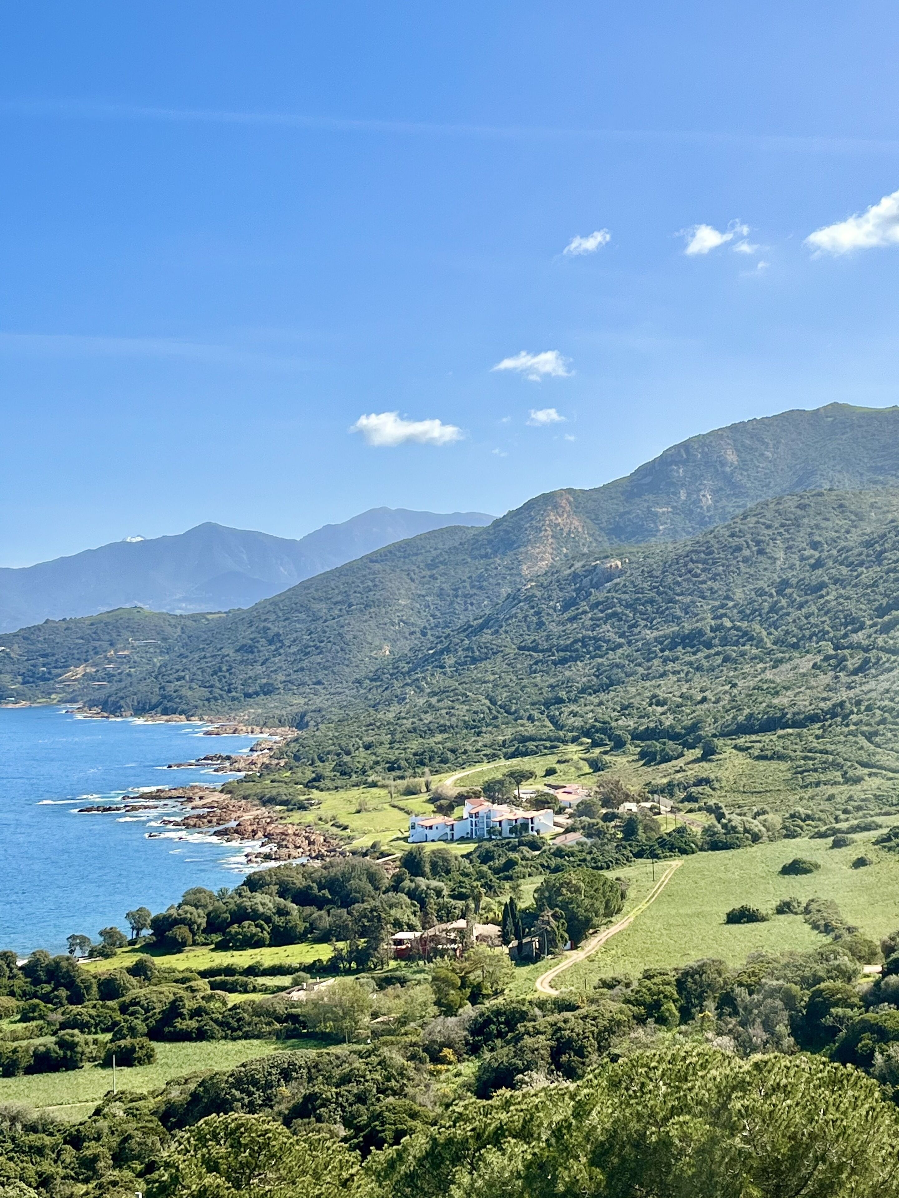 A coastal landscape with a view of the sea, green hills, and a few buildings.