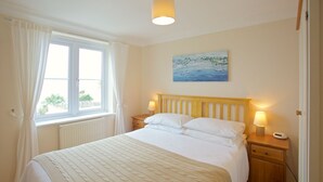 A bedroom with a bed, two bedside tables with lamps, a window with curtains, a painting on the wall, and a radiator under the window.