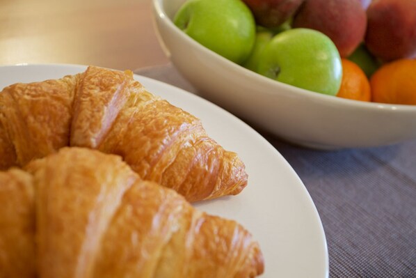 Une assiette de croissants et, au fond, un saladier rempli de fruits.
