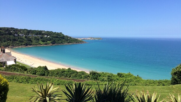 A coastal landscape with a beach, clear blue sea, and lush greenery.