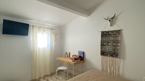 Un dormitorio con cama, escritorio, silla, televisión y un adorno en la pared.