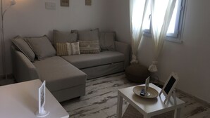 Una sala de estar moderna con un sofá gris, una mesa de centro blanca y una mesita auxiliar con un control remoto.
