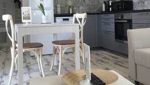 Una cocina moderna con armarios blancos, una zona de comedor con mesa blanca y sillas de madera, y un salpicadero de azulejos grises.