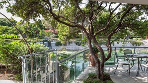 Un espace extérieur paisible, aménagé en patio, avec une balustrade en verre, une table et des chaises, et un arbre qui offre de l’ombre.