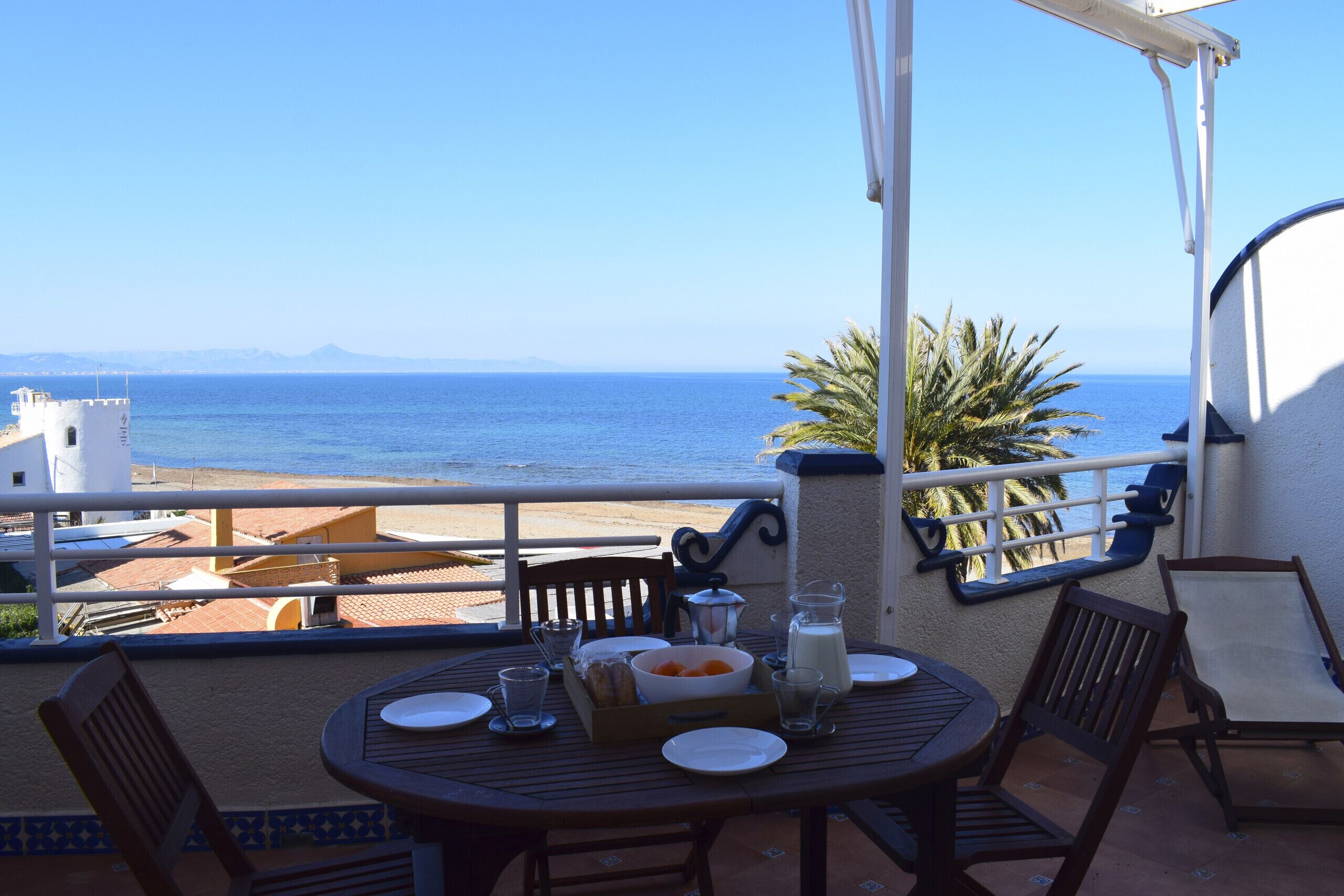 Ein Balkon mit Frühstückstisch, mit Blick auf den Strand und das Meer.