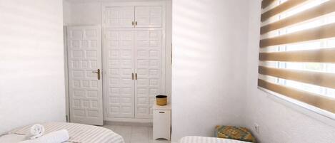 A bedroom with two beds, a wardrobe, a ceiling fan, and a window with blinds.