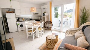 Een moderne keuken met witte kasten, een eethoek met een tafel en stoelen, en een zithoek met een bank en uitzicht op de omgeving.