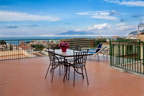 A balcony with a table and chairs, a potted plant, and a view of the sea and a mountain. - Panoramic Penthouse with Breathtaking Views & Private Terrace in Sorrento Center (Sorrento)