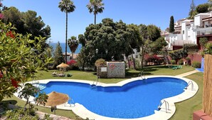 Ein Pool mit Steinstruktur, umgeben von viel Grün und Blick aufs Meer.